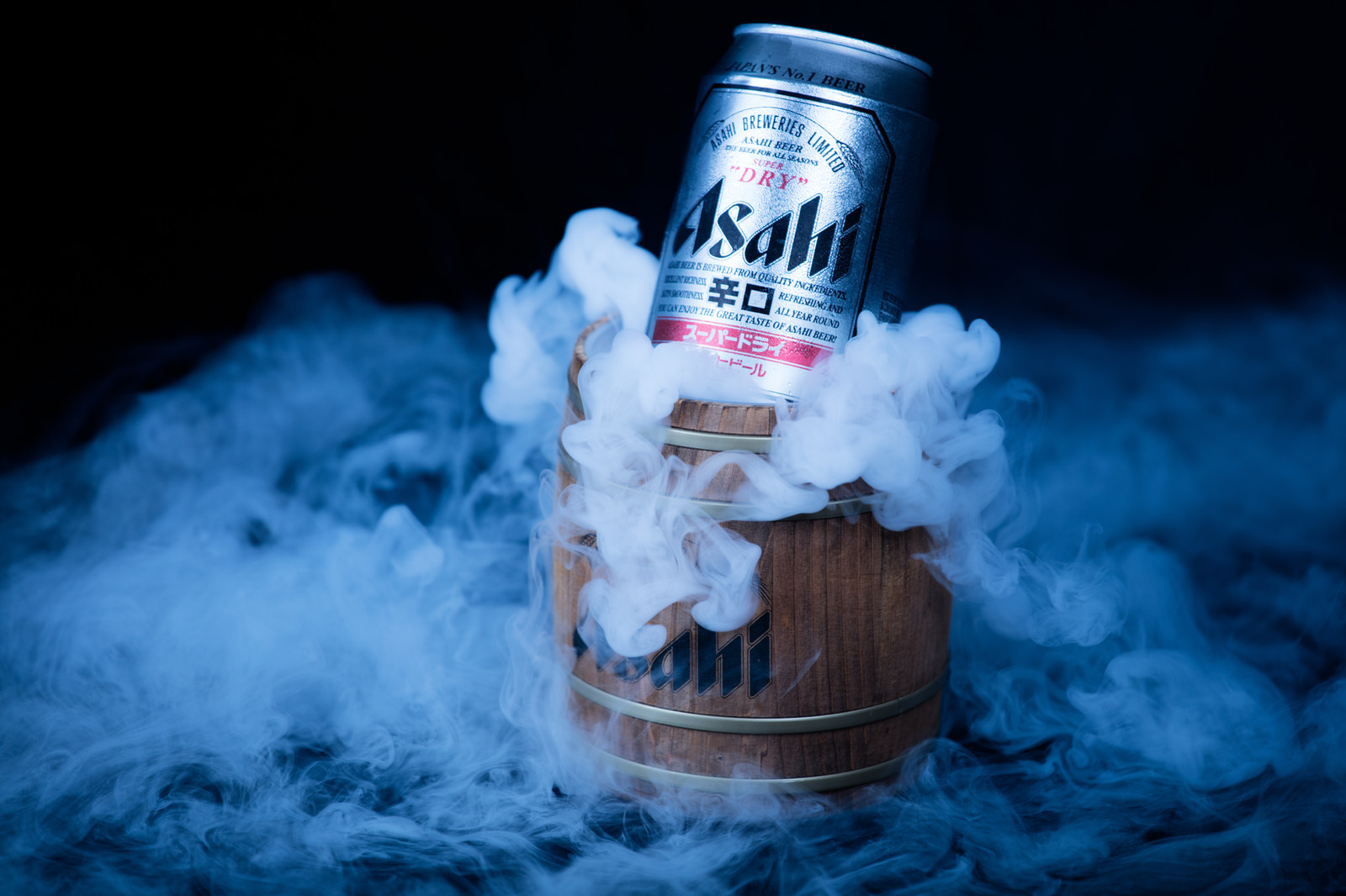 Asahi beer can on a wooden barrel surrounded by blue-lit smoke