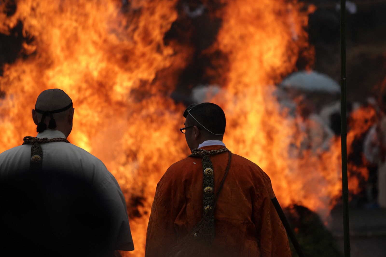 Two figures seen from behind in front of a large fire