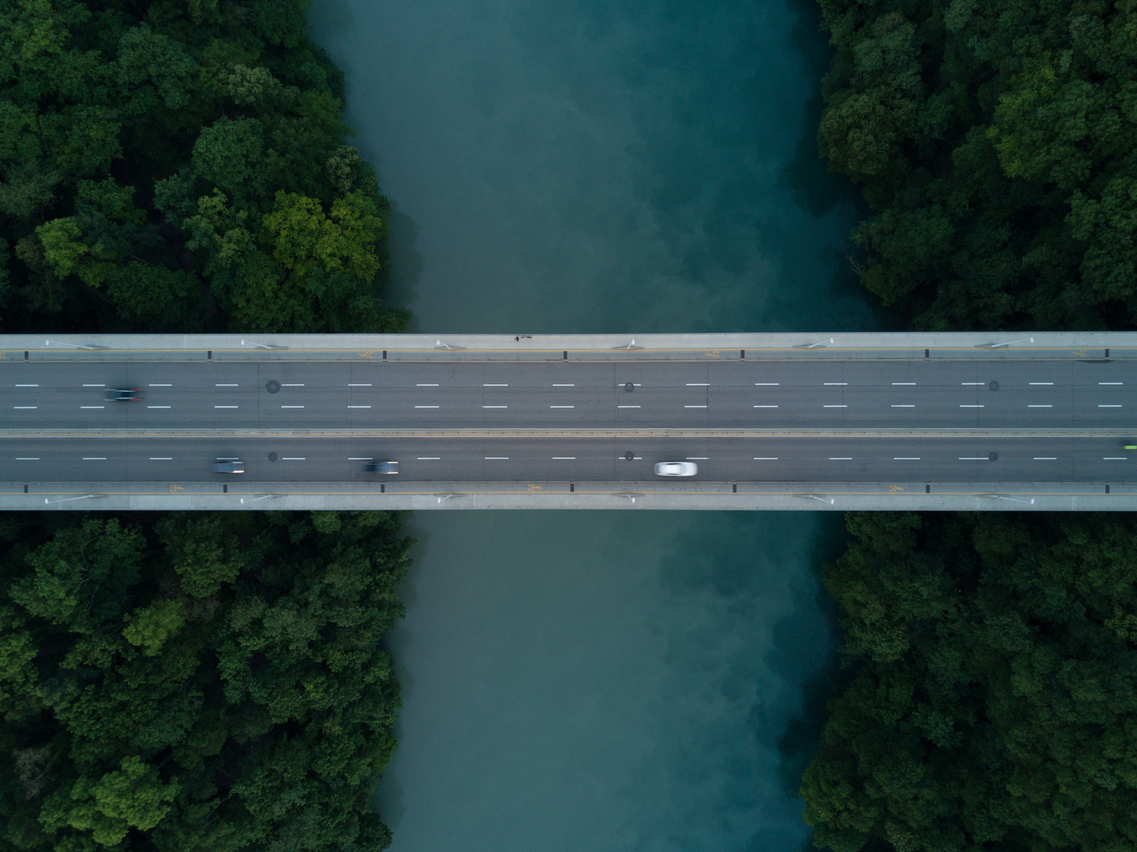 Overhead view of a bridge crossing a blue river surrounded by trees